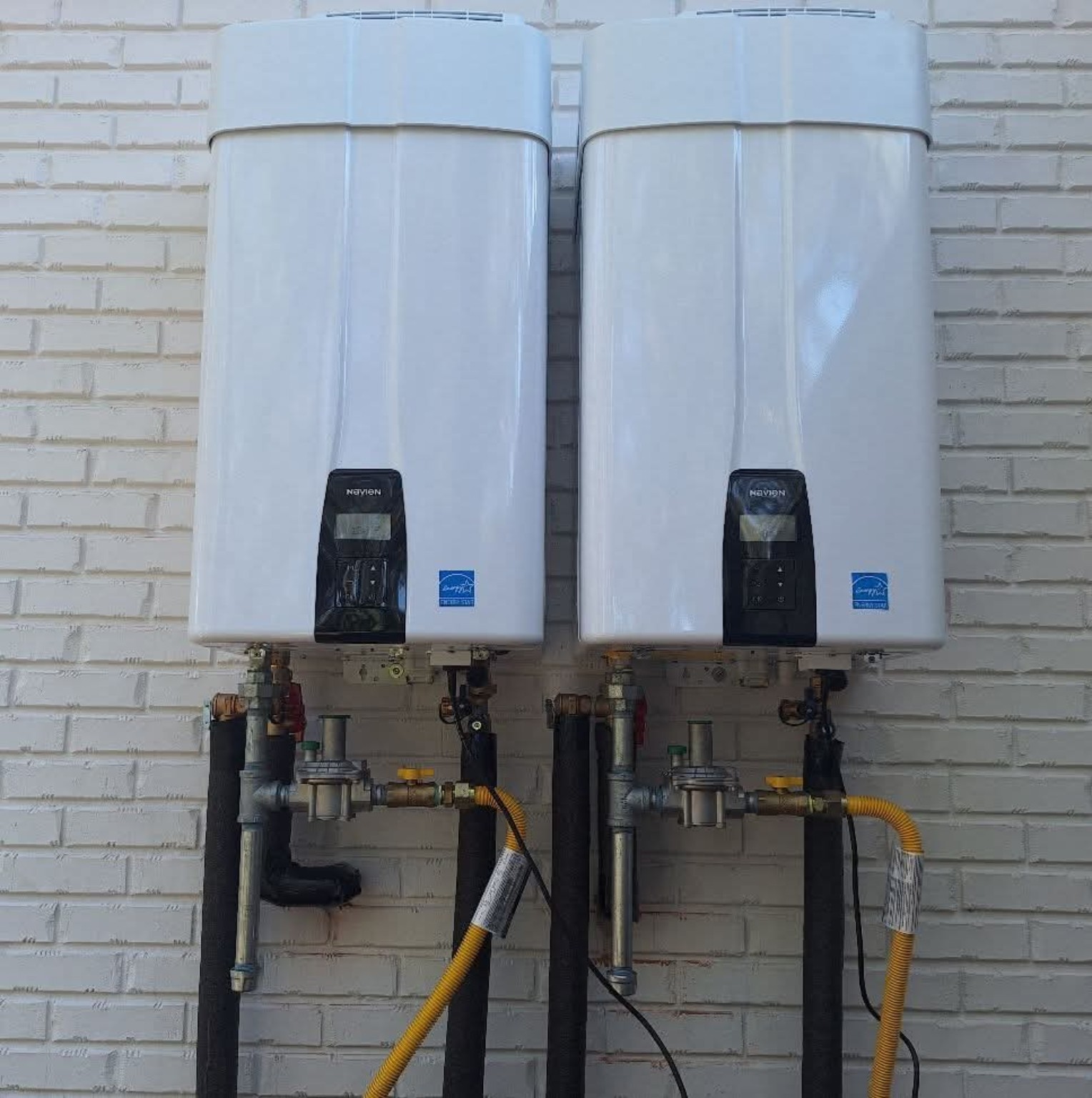 Two Navien tankless water heaters installed side by side on exterior brick wall